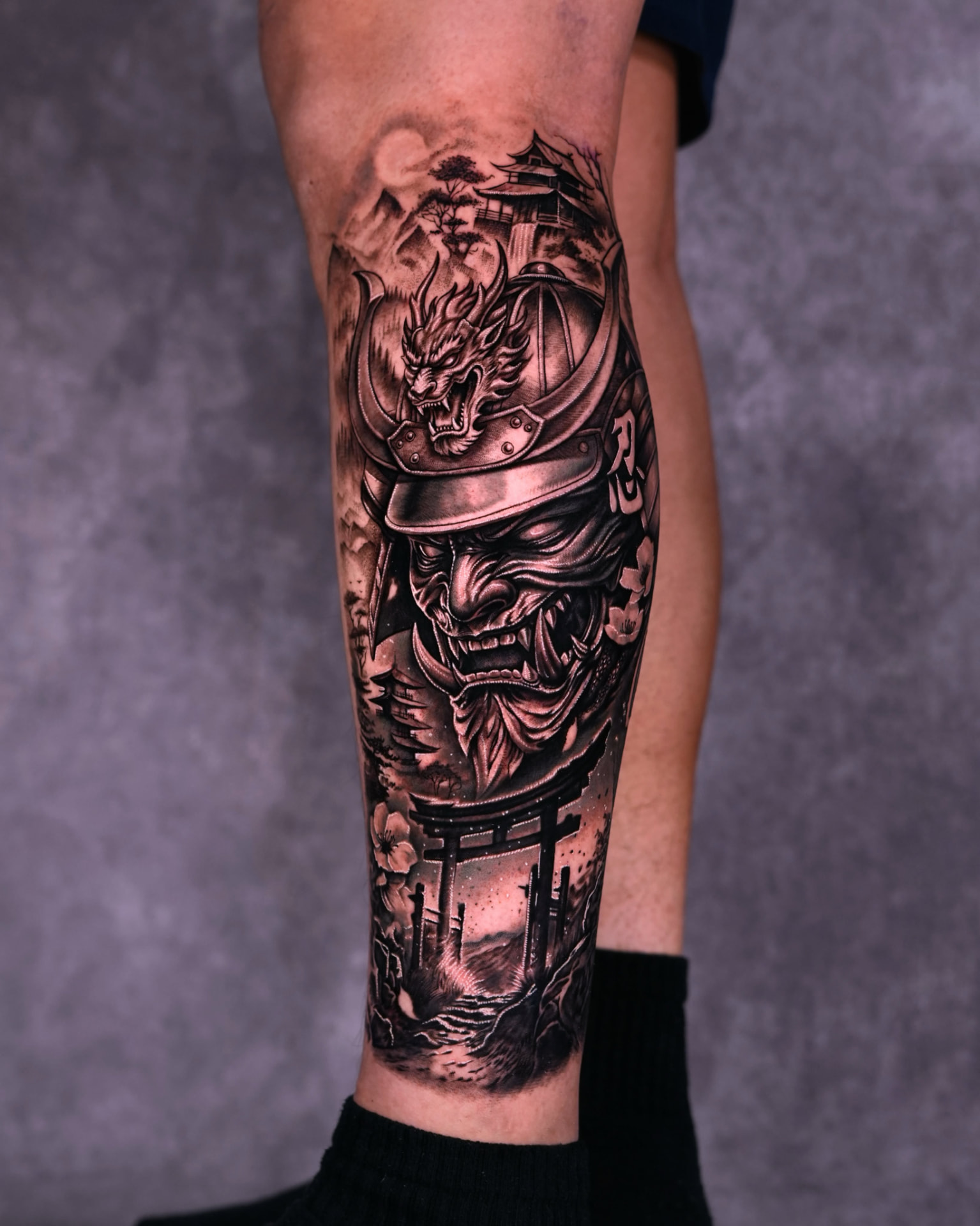 Black and grey Japanese samurai mask and dragon leg sleeve tattoo by Lions Ink
